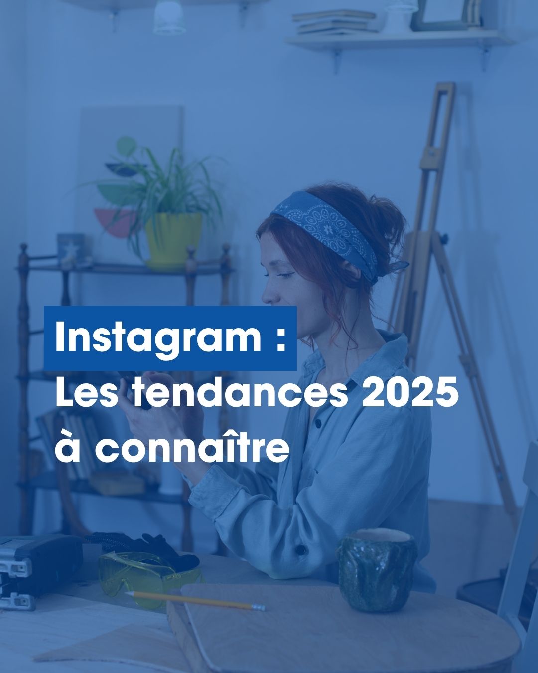 Portrait d'une jeune femme assise dans un atelier de peintre, utilisant son smartphone.